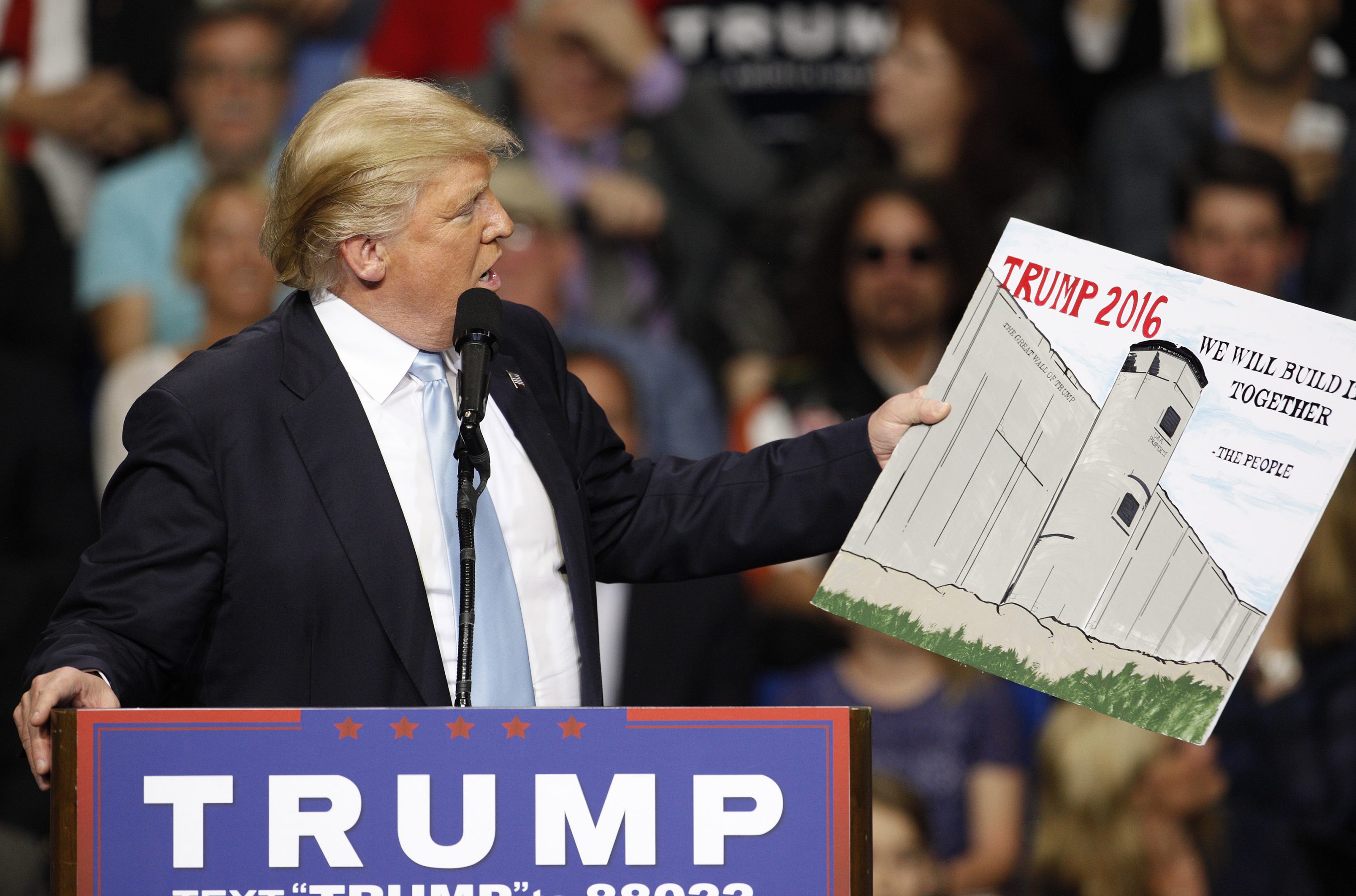 Donald Trump em sua campanha presidêncial em 2016, usou um poster feito por um apoiador na audiência enquanto aprestava seu plano para construir o muro na fronteira com o México