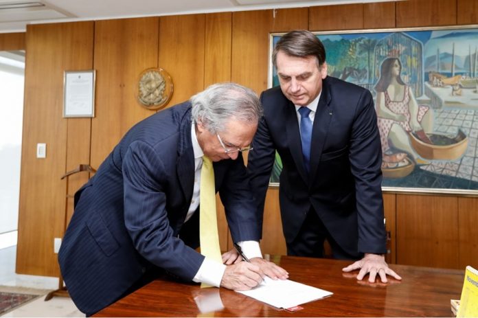 Ministro Paulo Guedes assina documento ao lado do presidente Jair Bolsonaro (Foto Facebook Jair Bolsonaro)