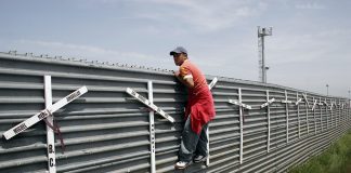 Homem escala muro na fronteira fronteira Tijuana-San Diego. As cruzes representam as mortes por tentativas fracassadas (Foto: Tomas Castelazo/Wikimedia)
