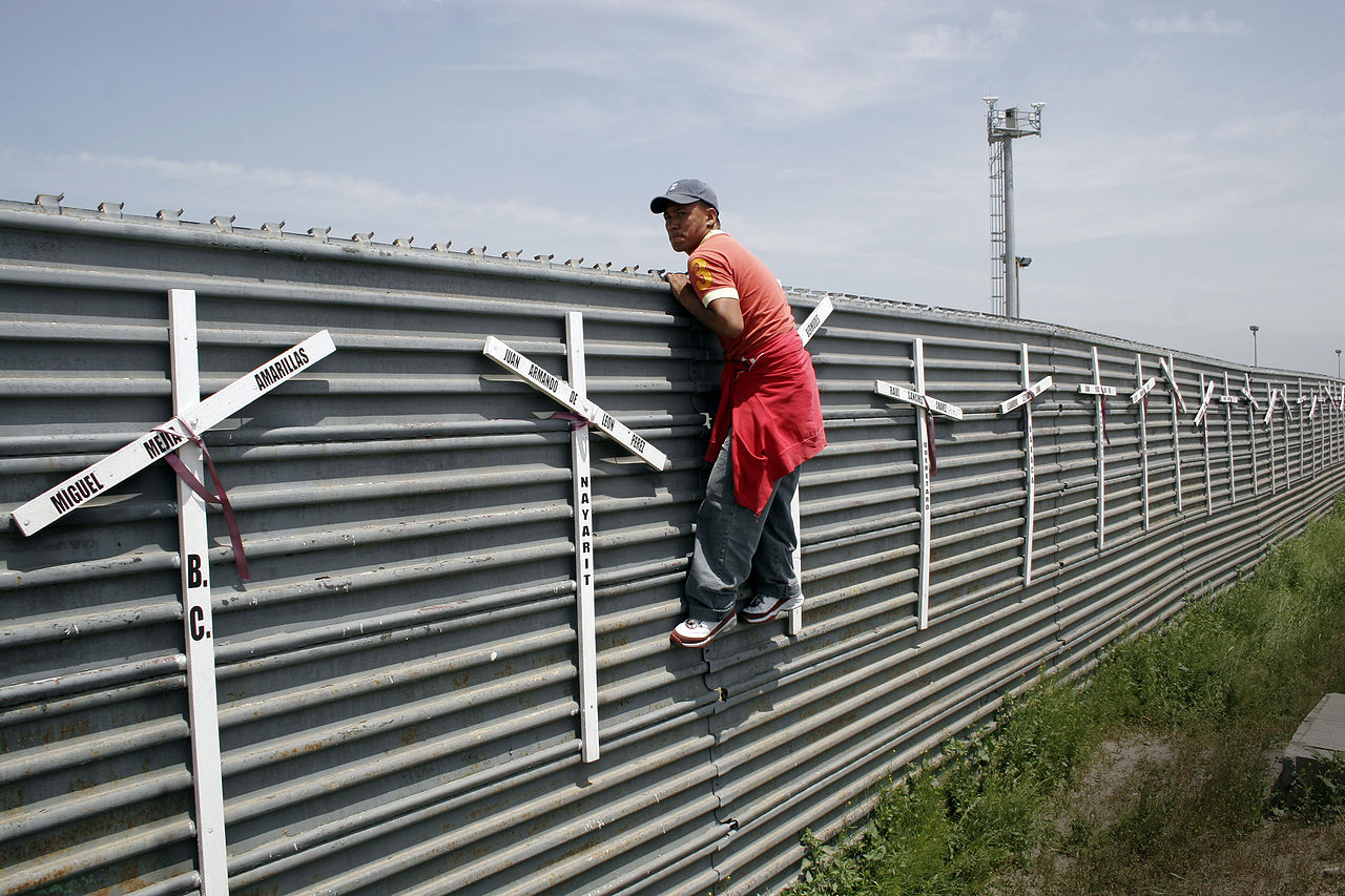 Homem escala muro na fronteira fronteira Tijuana-San Diego. As cruzes representam as mortes por tentativas fracassadas (Foto: Tomas Castelazo/Wikimedia)