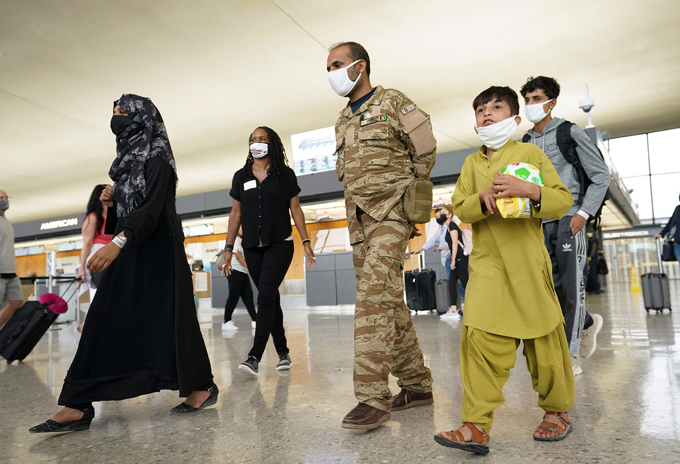 Família de afegãos caminha em direção a um ônibus que leva refugiados a um centro de processamento após sua chegada ao Aeroporto Internacional de Dulles, Virgínia (Foto: REUTERS/Kevin Lamarque)