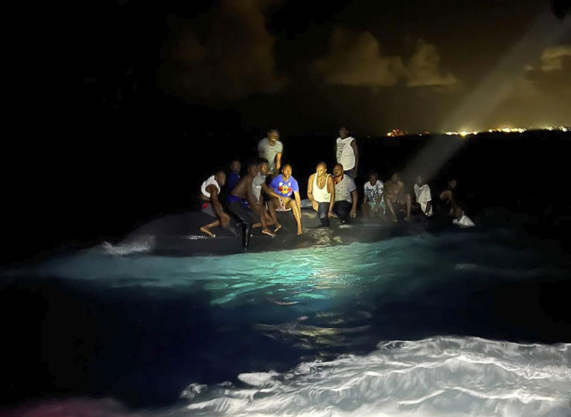 Sobreviventes sentados em um barco virado enquanto estão prestes a ser resgatados perto de New Providence, nas Bahamas (Foto: Royal Bahamas Defense Force via AP)