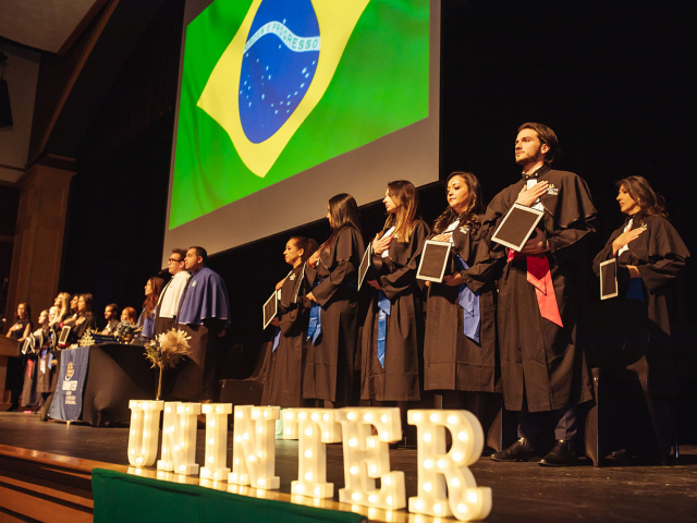 Emocionados, os graduados acompanham o hino nacional do Brasil